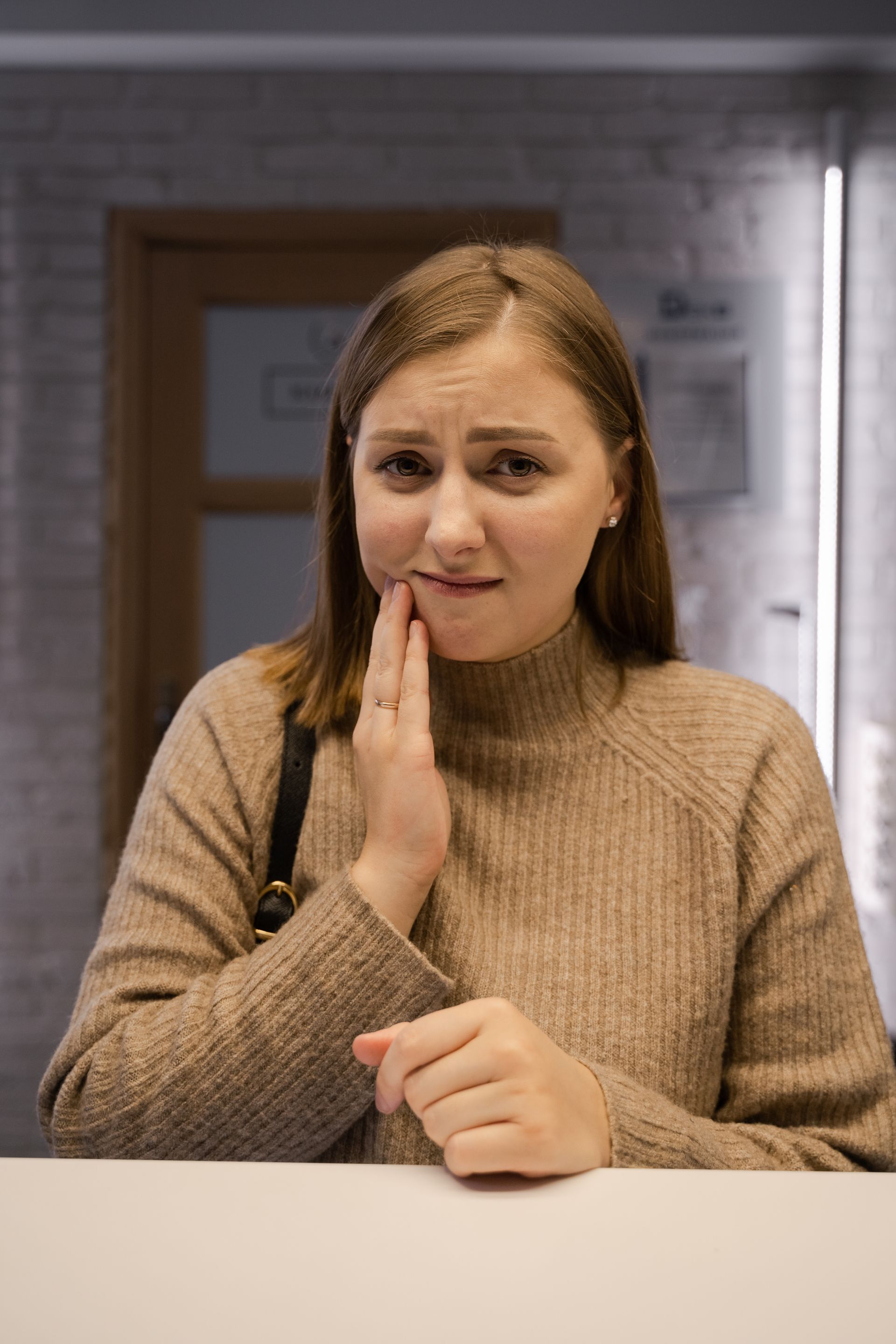 Woman with tooth pain holding jaw before emergency dental visit